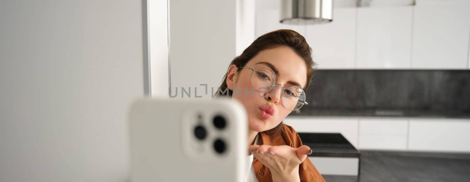 Close up portrait of woman taking selfie, sending air kiss at mobile camera, taking picture on smartphone.