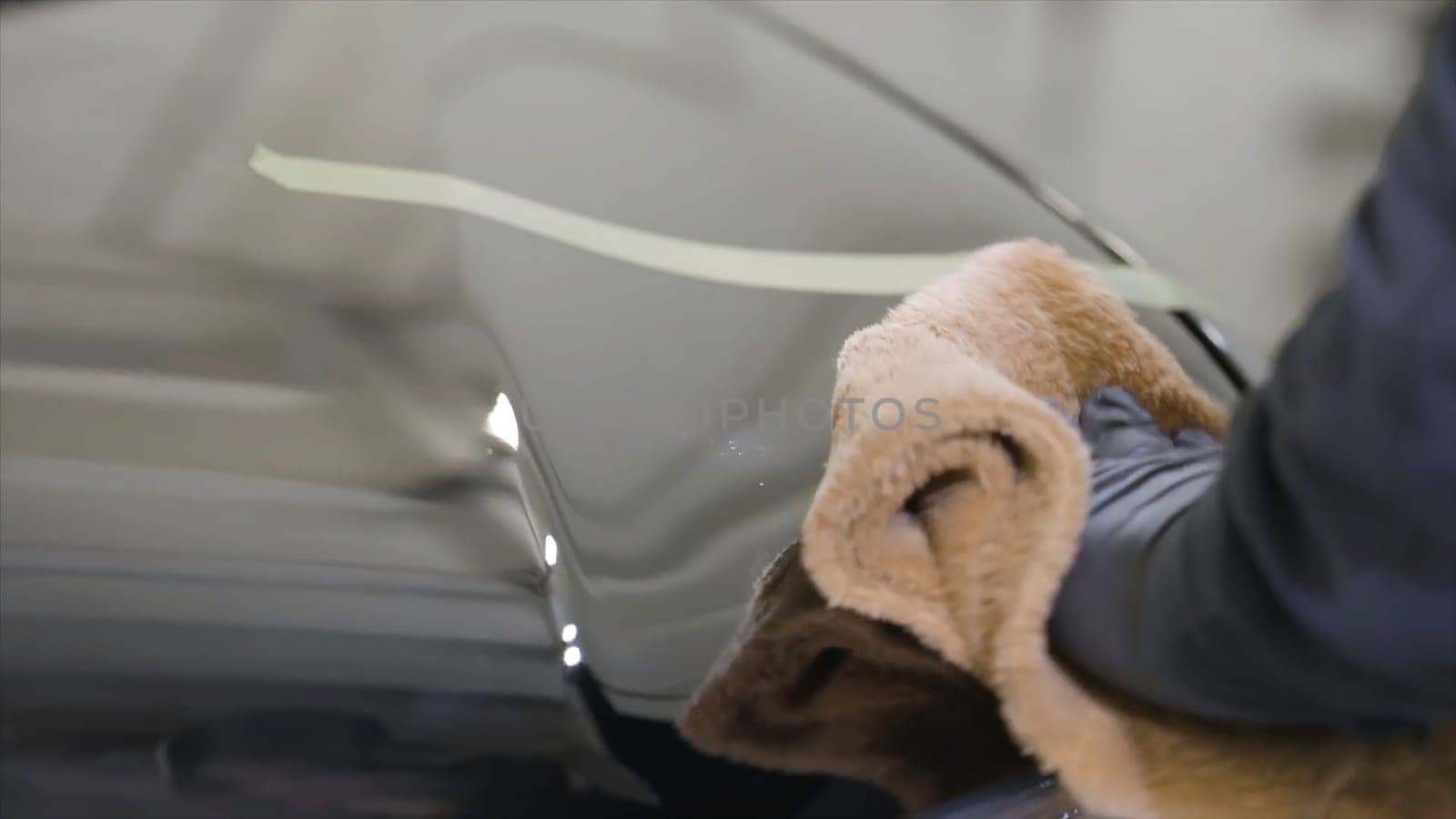 Close up for man hand in black glove washing a car window in a car wash, cleaning service. Car care service worker using microfiber cloth for cleaning a car.