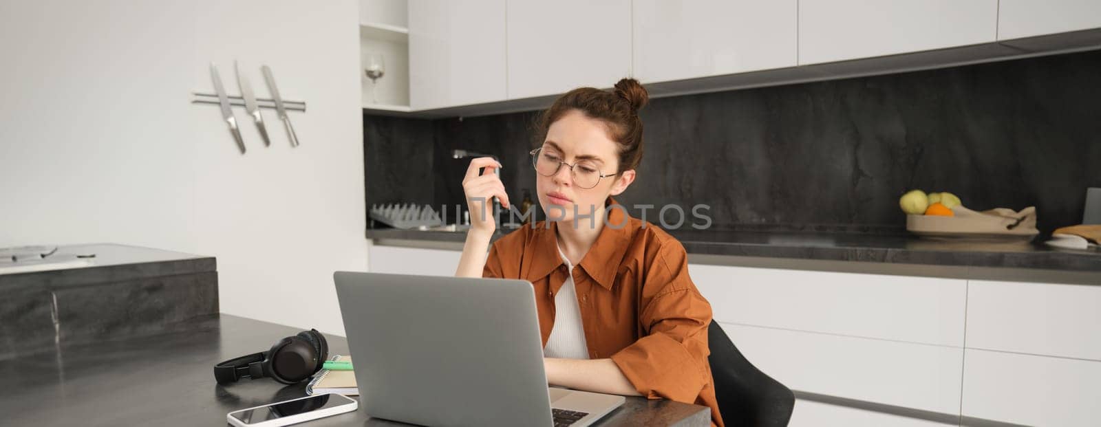 Portrait of woman with serious face, sitting in front of computer, using laptop, working from home, looking at screen with thoughtful face.