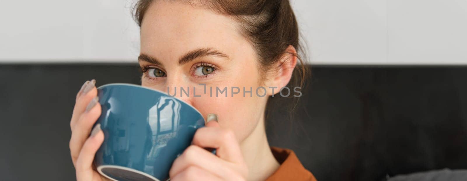 Close up portrait of beautiful, relaxed young woman, enjoying aroma of coffee, drinking cappuccino and smiling. Lifestyle and people concept