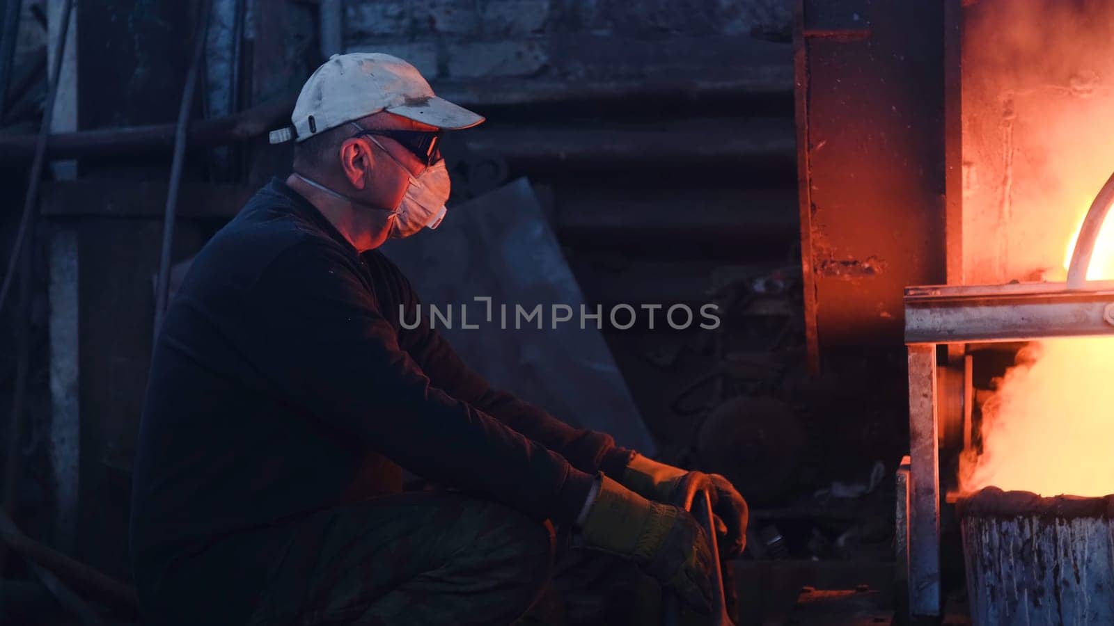 Workers at metallurgical plant working with hot metal. Stock footage. Workers in uniforms and helmets work with dangerous hot metal at high temperatures in old metallurgical factory.