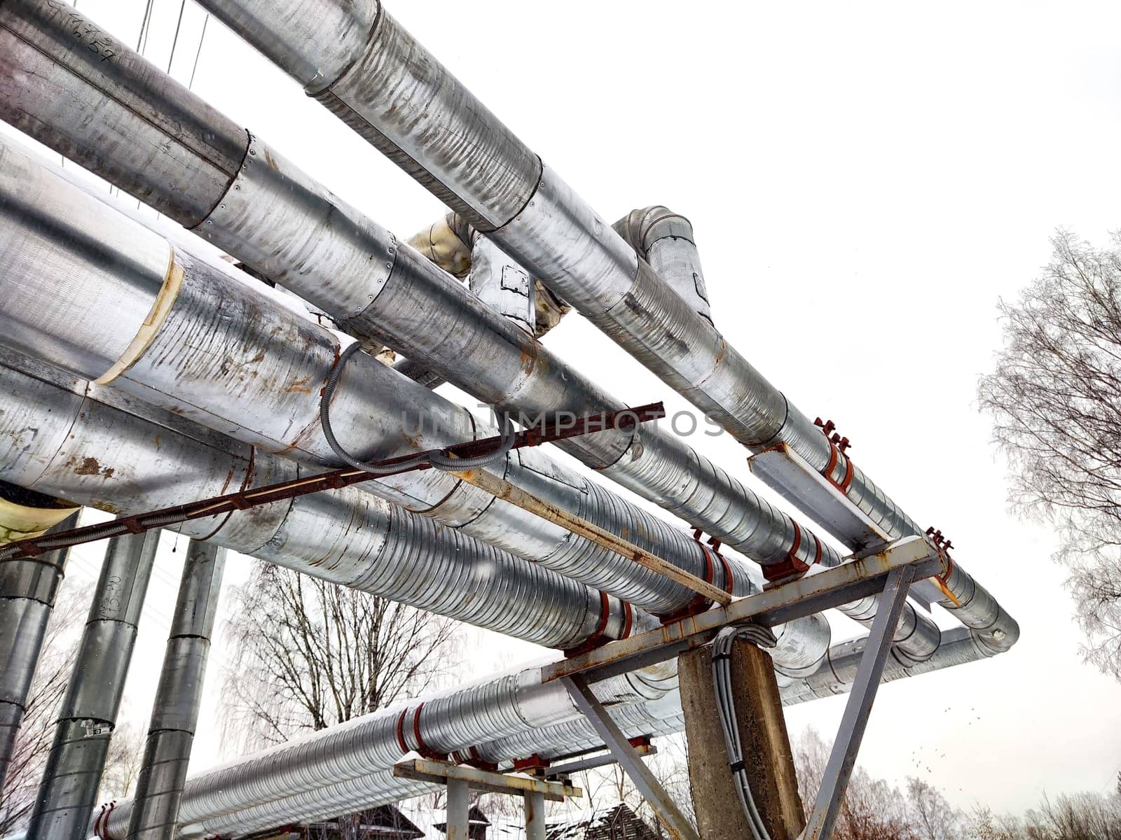 Metal pipes in thermal insulation winding outdoors and the over-illuminated white sky on background