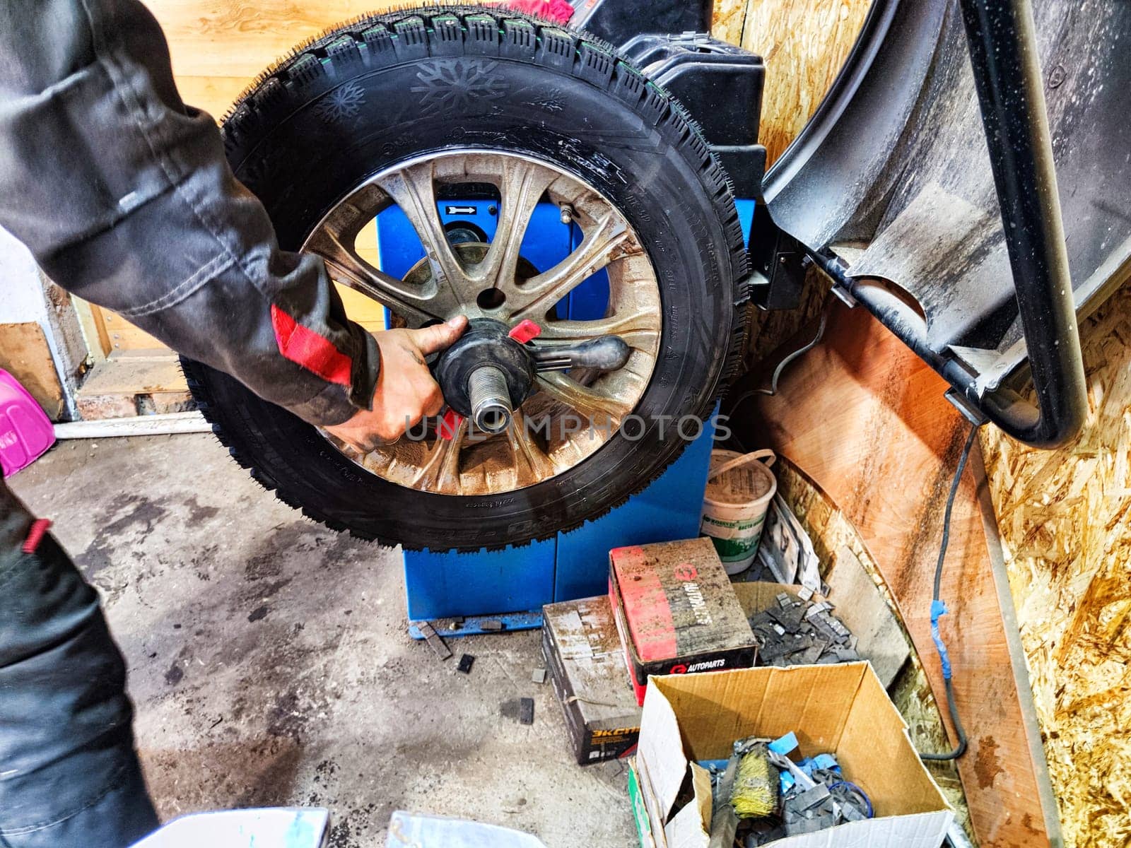 Ishim, Russia - November 27, 2023: A mechanic repairs a car wheel and makes a tire in a dirty garage. Replacement of summer wheels, tires for winter indoors by keleny