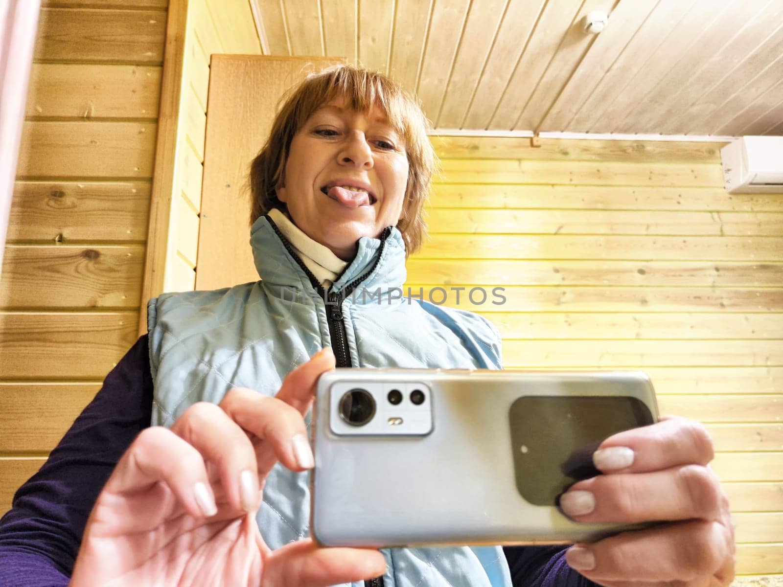 Middle-aged woman using smartphone for selfie and blogging. Female blogger poses in a photo. The girl admires herself in the mirror