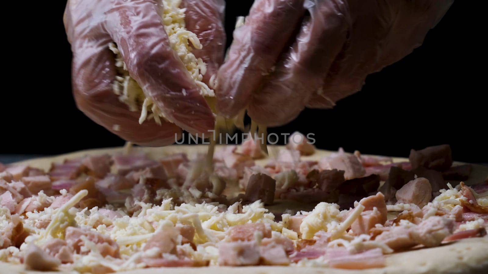 A female hands in cooking gloves sprinkling pizza with grated cheese, italian food concept. Close up for chef hands putting cheese on the pizza.