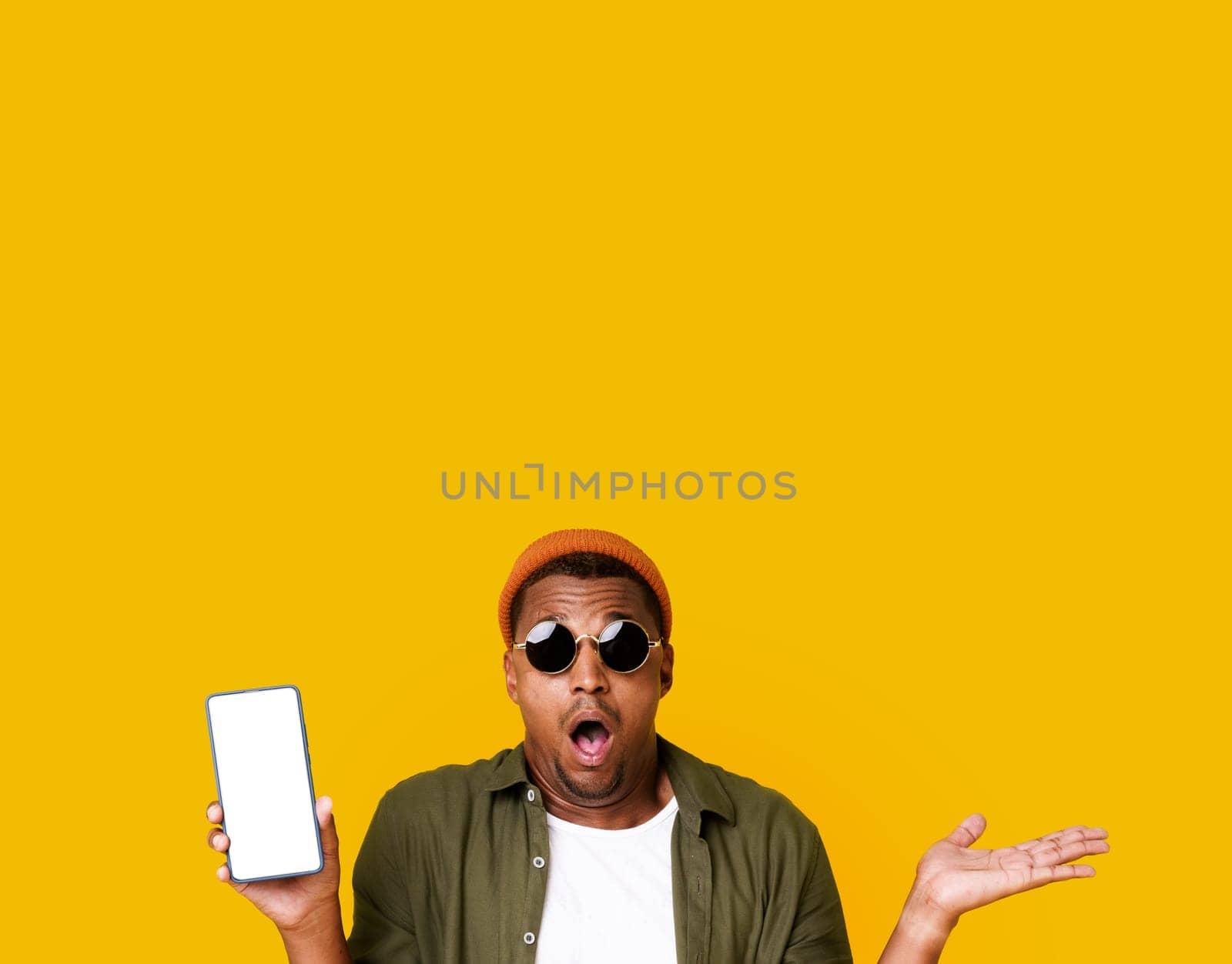 Exited African American Man In Trendy Glasses In Mobile App Advertisement Isolated Over Yellow Color Background. Young Smiling Cheerful Satisfied Positive Happy Black Man 20s In Casual Basic Closing With Mobile Phone. High Quality Photo