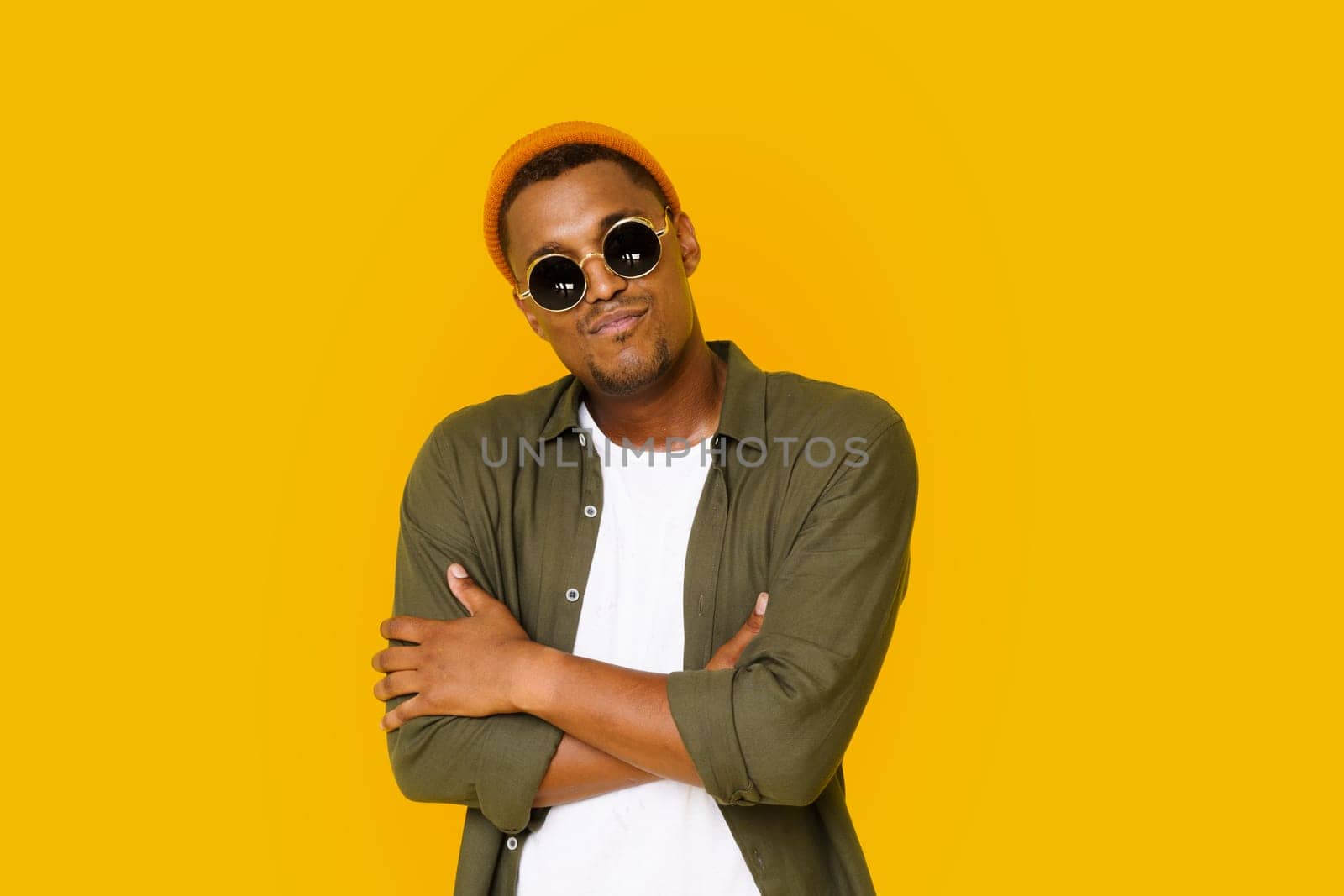 Confident Trendy Handsome Man 20s In Basic Closing With Crossed Hands. Young Expertise In Business Concept. Studio Shot Of Cool Clever Intelligent Executive Man Isolated Over Yellow Background. by LipikStockMedia