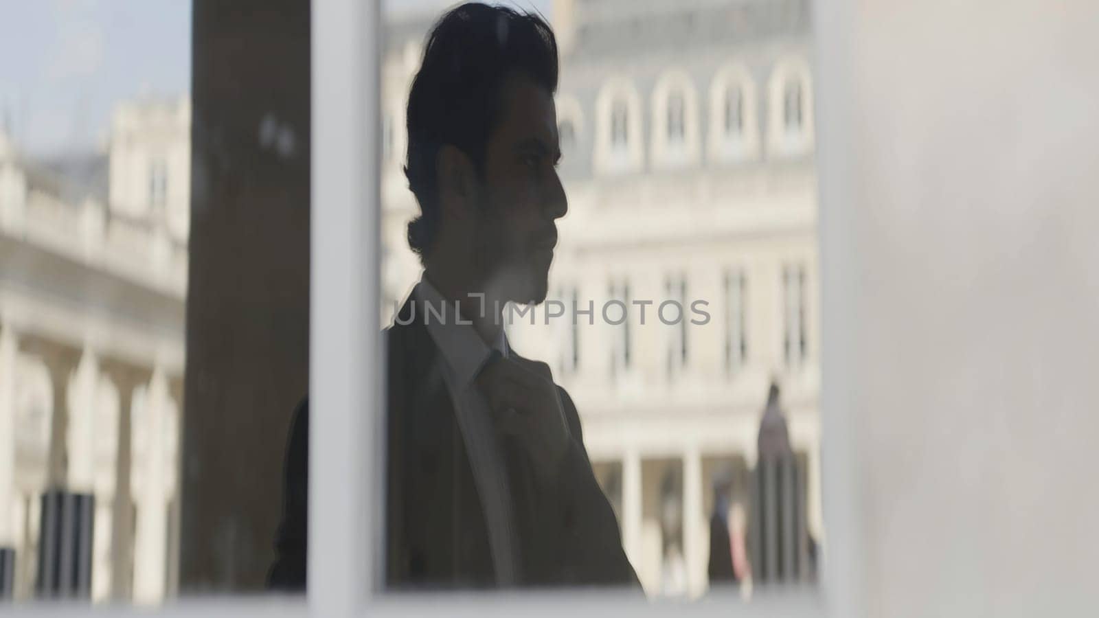 Attractive businessman in black suit thinking while standing outside on the street. Action. Man reflection in glass window near antique building