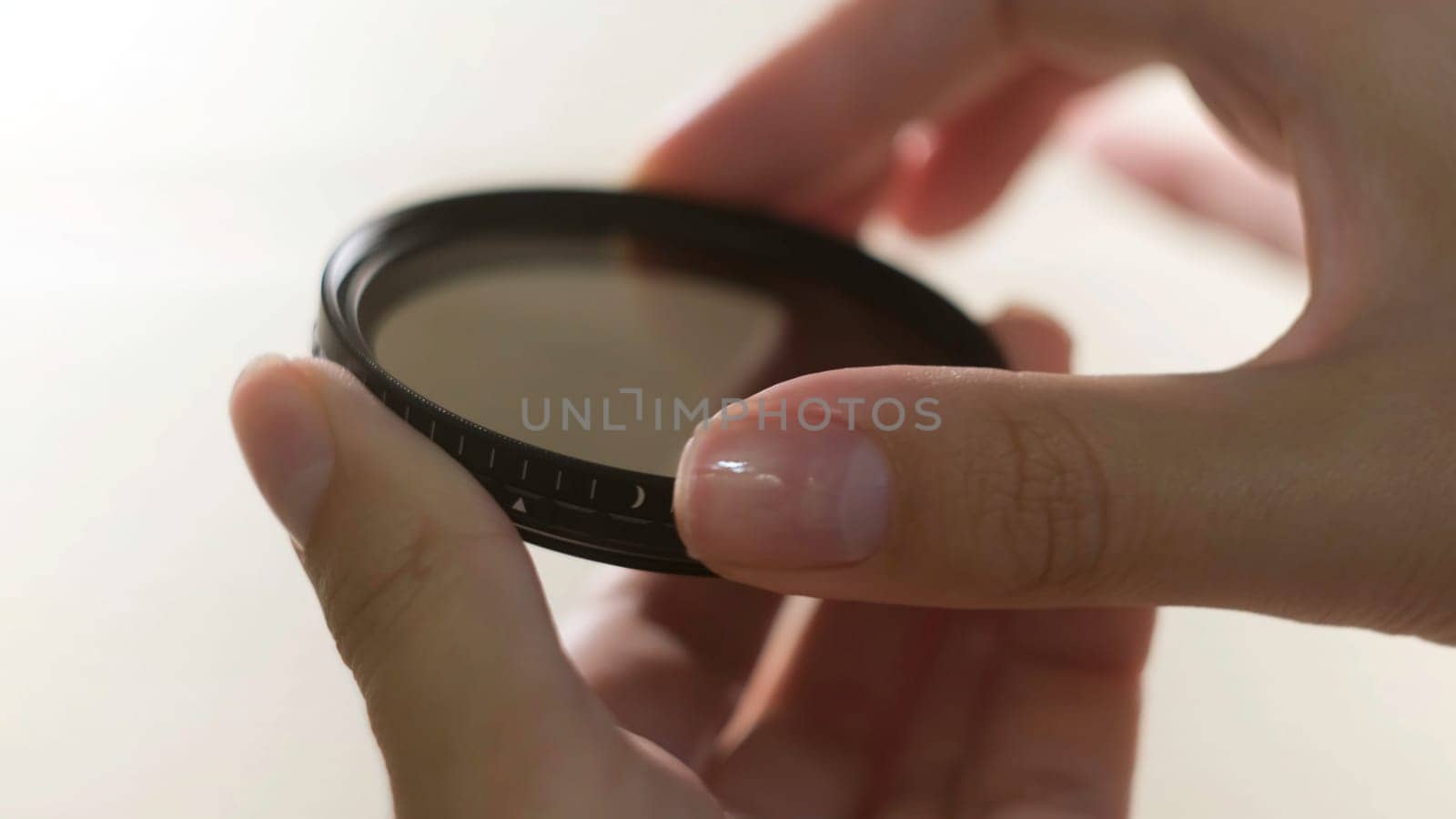 Close up of polarizing lens filter in girls hands isolated on white background. Woman turning into the both sides mechanism of lens filter.