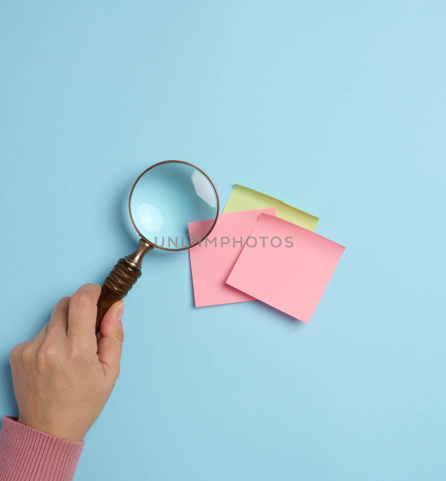Empty paper stickers adhered to a blue background, and a female hand with a magnifying glass on a blue background