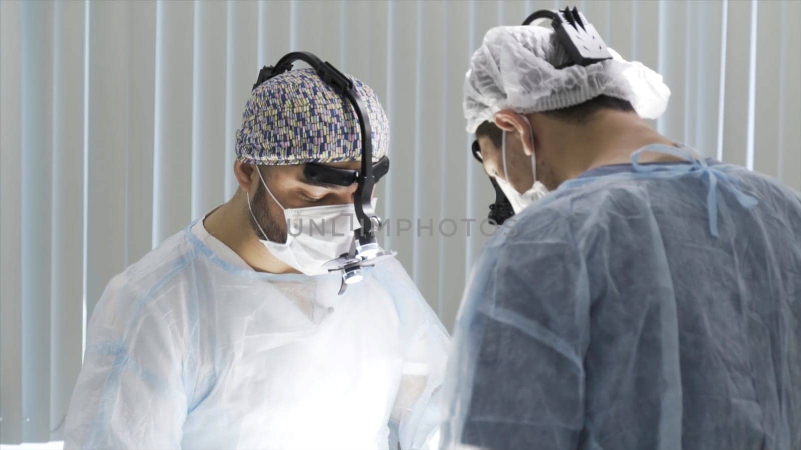 Two surgeons working at the operating clean room. Two male doctors wearing sterile uniform and binocular loupe while performing surgery, concept of health care and medicine.