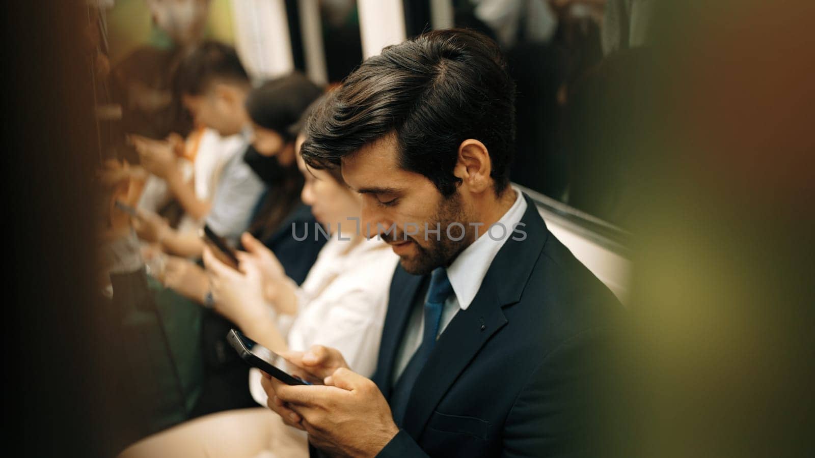 Smiling caucasian business man looking at mobile phone or playing social media while sitting in train. Attractive project manager going to work place by using public transport in rush hour. Exultant.