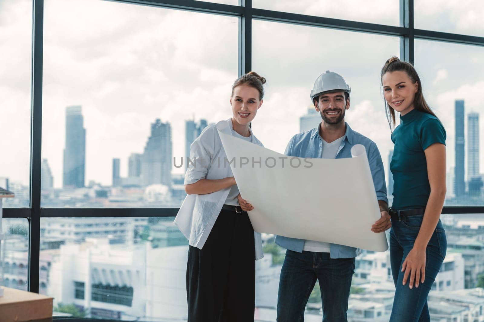 Group of smart architect engineer looking at camera while holding project plan. Skilled manager team discuss about building construction while standing near with city view. Team working. Tracery.