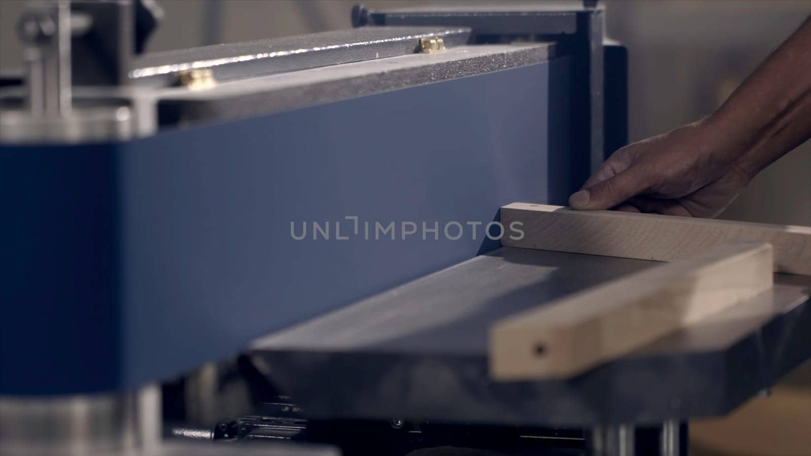 Close-up of man grinds wood products on industrial machine. Action. Carpenter polishes wooden product for tape manufacturing machine.