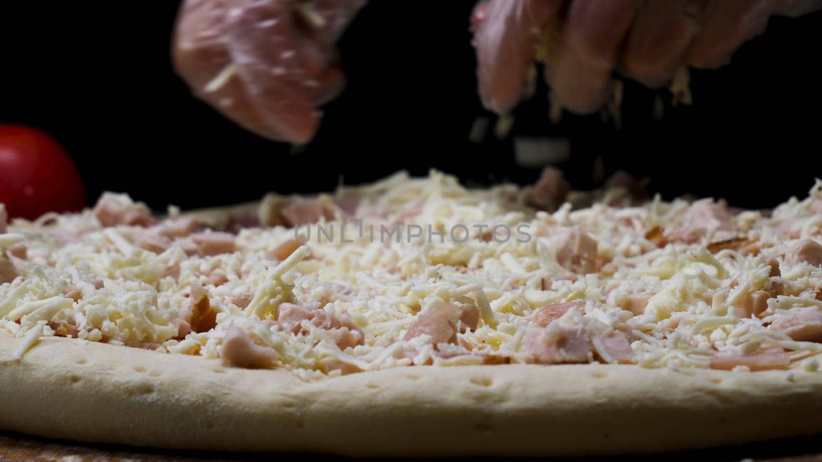 A female hands in cooking gloves sprinkling pizza with grated cheese, italian food concept. Close up for chef hands putting cheese on the pizza.