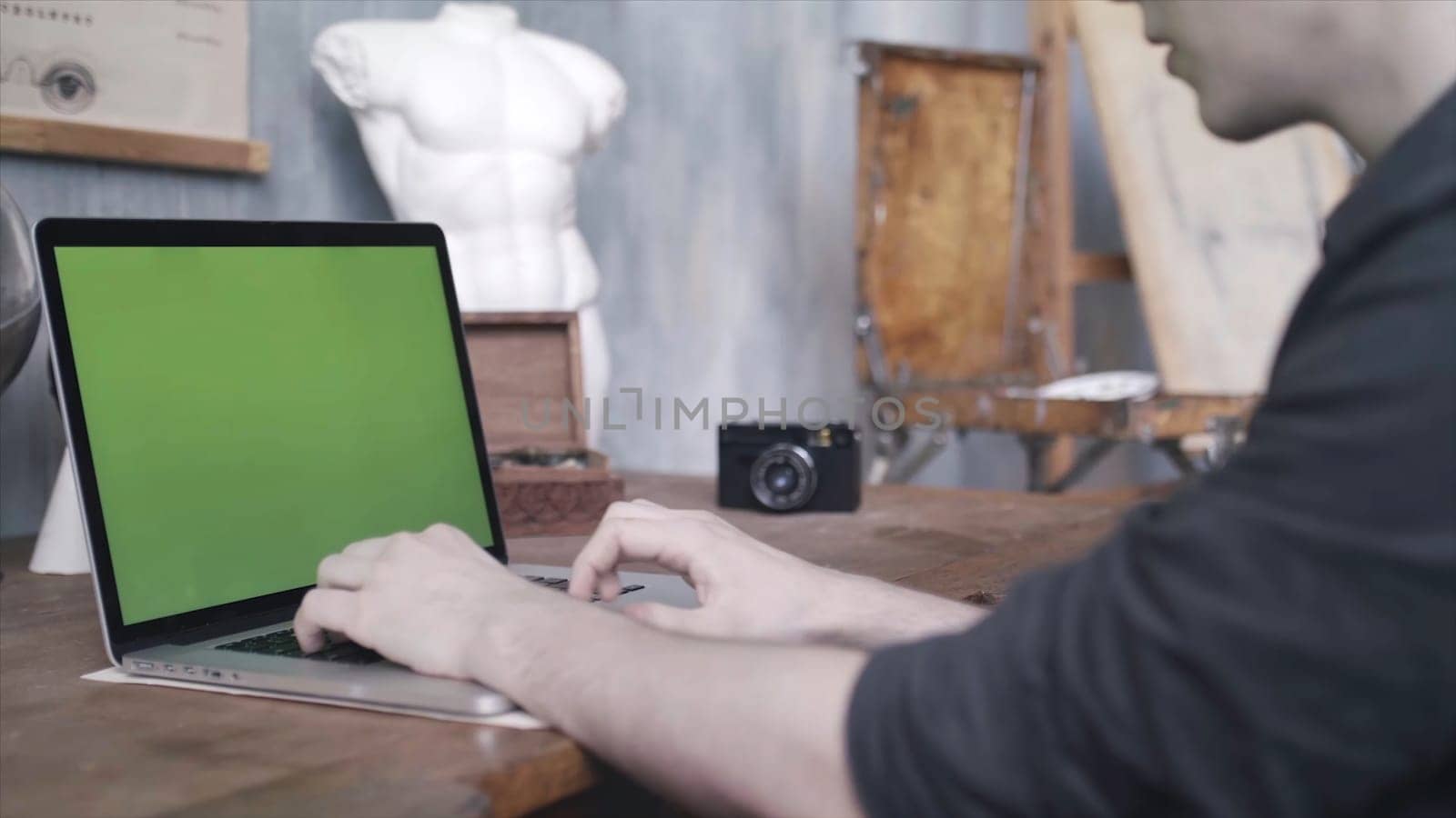 Close-up of man in black shirt sitting at the old table and typing on laptop with green chroma key screen. Laptop new technology concept, chroma key green screen