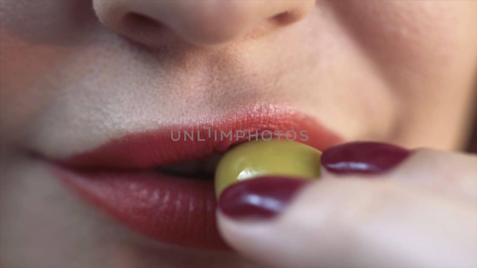 Close up of red sexy lips of a woman biting a green olive. Sensitive red lips, extreme close up of facial details of a young woman with beautiful skin.