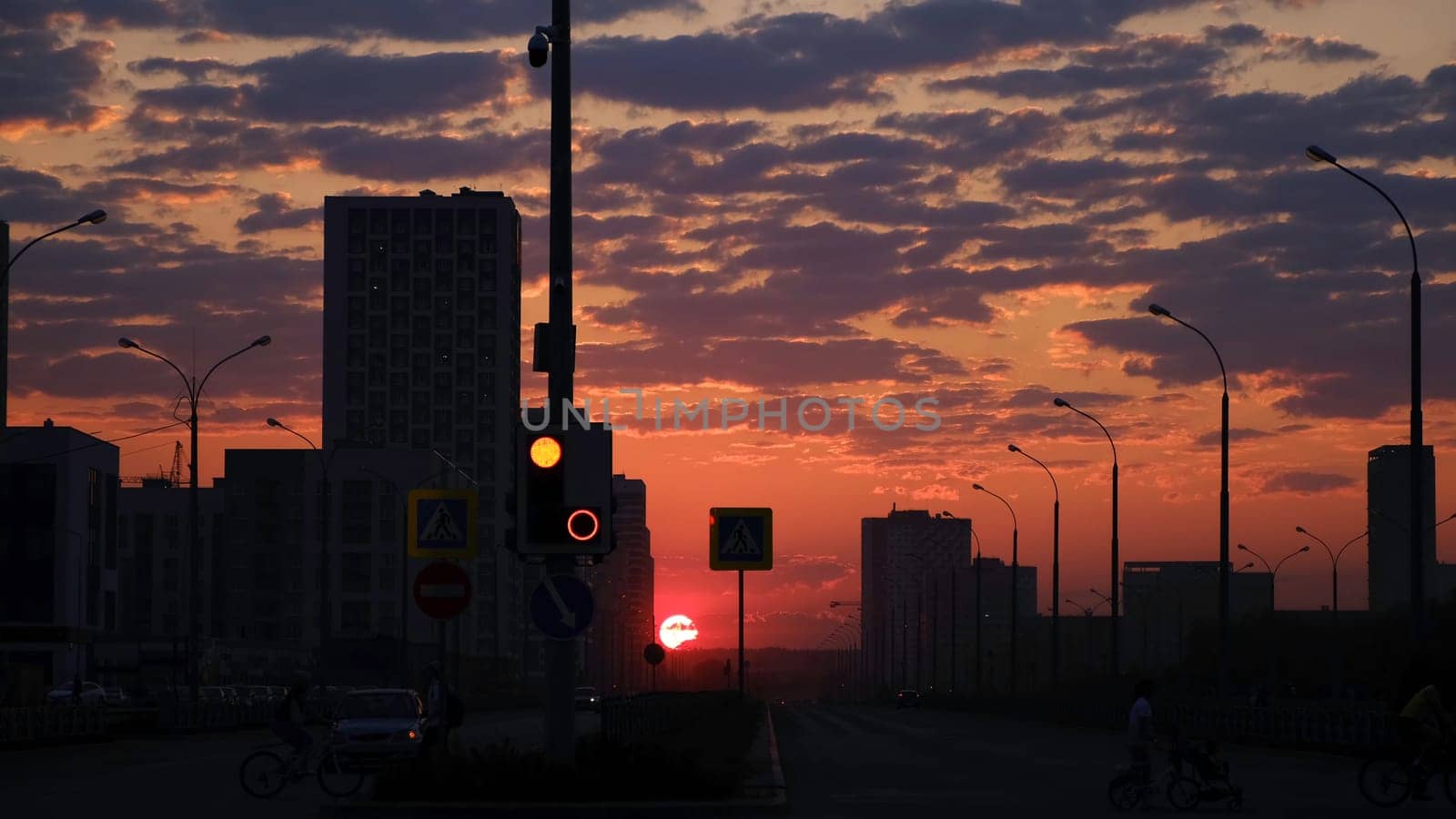 Early morning sunrise in a city street. Breathtaking pink and orange sky with bright red shining sun rising above the dark city with walking people and driving cars.