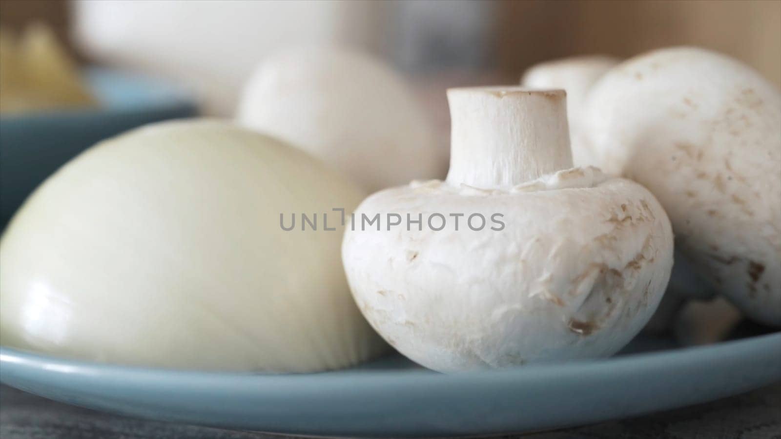 Close up of fresh mushrooms and cut onion lying on glass plate. White raw champignons and onion, ingredients prepared for cooking, food concept.
