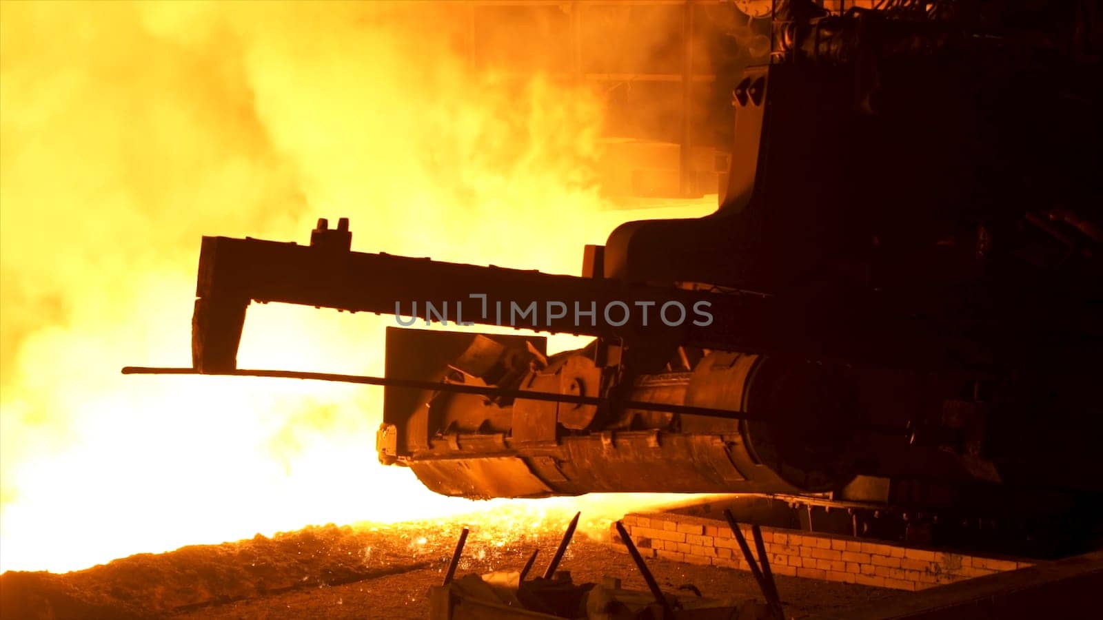 Molten metal pouring from the special mechanism, metallurgy concept. Molten steel flowing in metallurgical chute behind moving mechanism