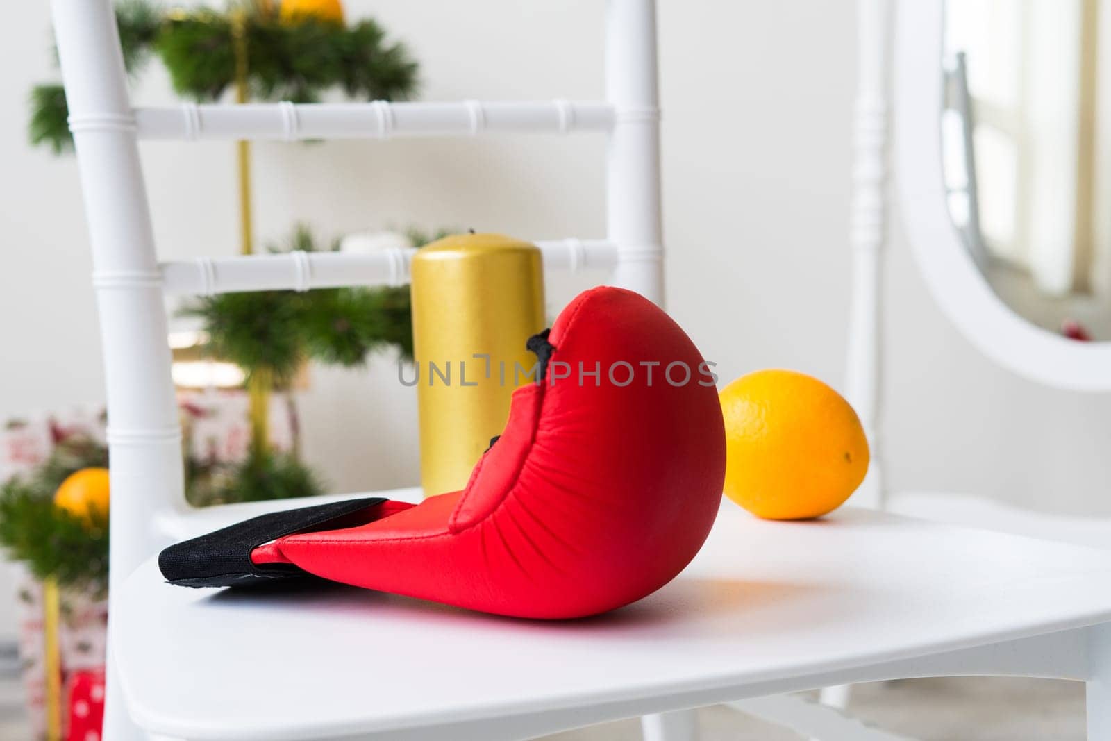 Sports equipment: dumbbell, boxing gloves, fir branch, Christmas ornament, gifts on a chair.