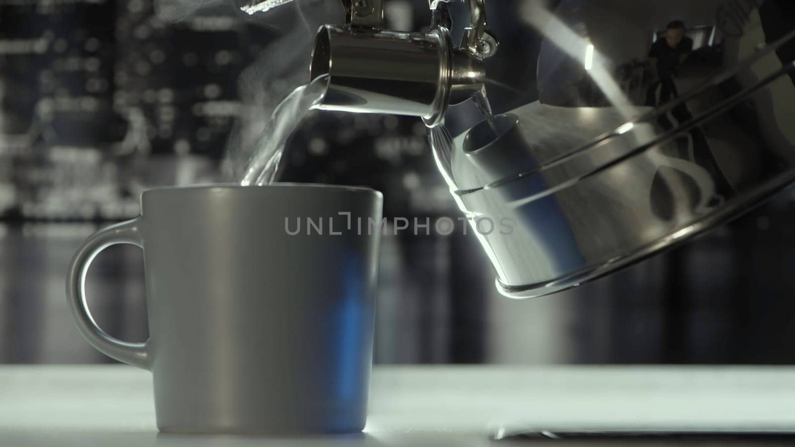 Close up of pouring hot boiled water from the polished steel gas kettle into the mug. Action. Cozy atmosphere in the kitchen in grey colors at home