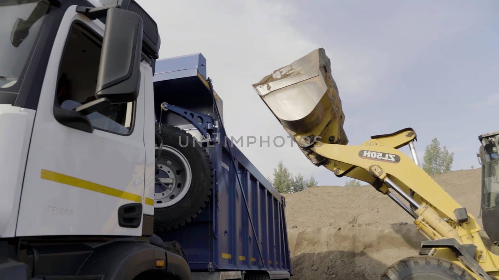 Germany - Berlin, November 20, 2022: Excavator in action at the construction site. Scene. Excavator flipping the bucket of yellow color loaded with sand, loading the truck with sand