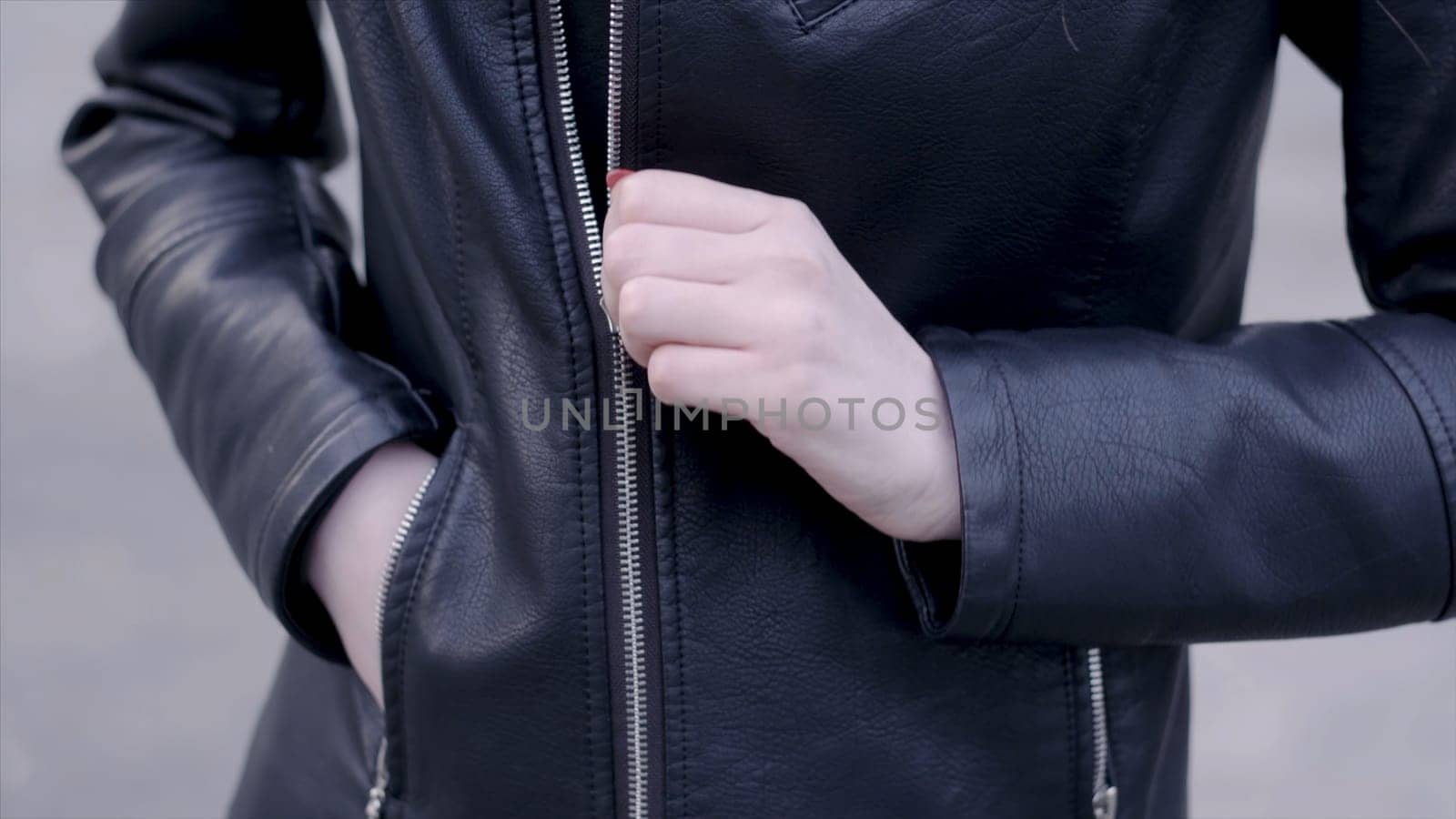 Woman wearing trendy black leather jacket with zipper. Action. Young woman zips leather jacket.