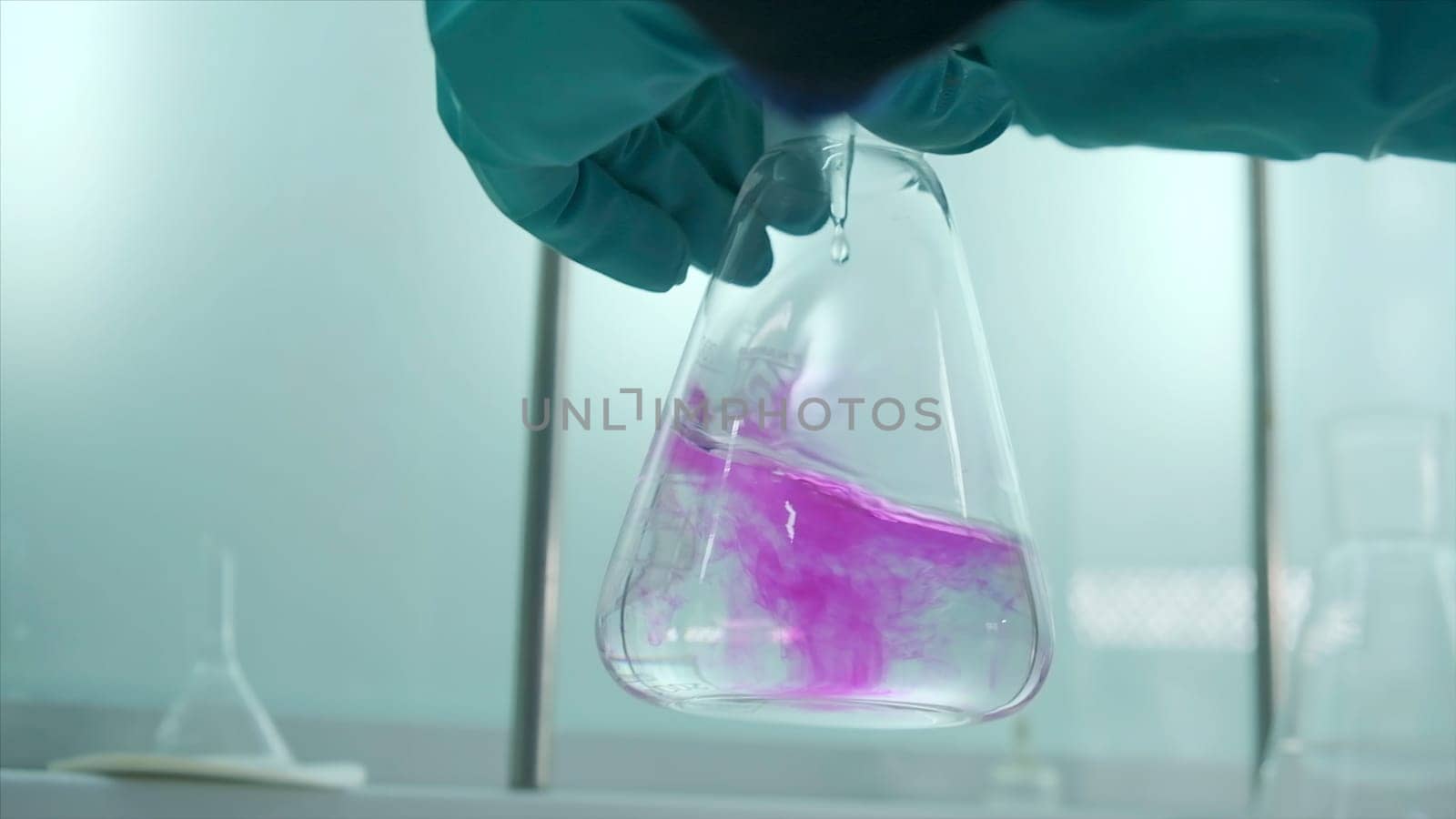 Close-up of flask with chemical liquid. Clip. Laboratory assistant conducts experiments with chemical liquid that changes colors. Chemical process in transparent flask in laboratory.