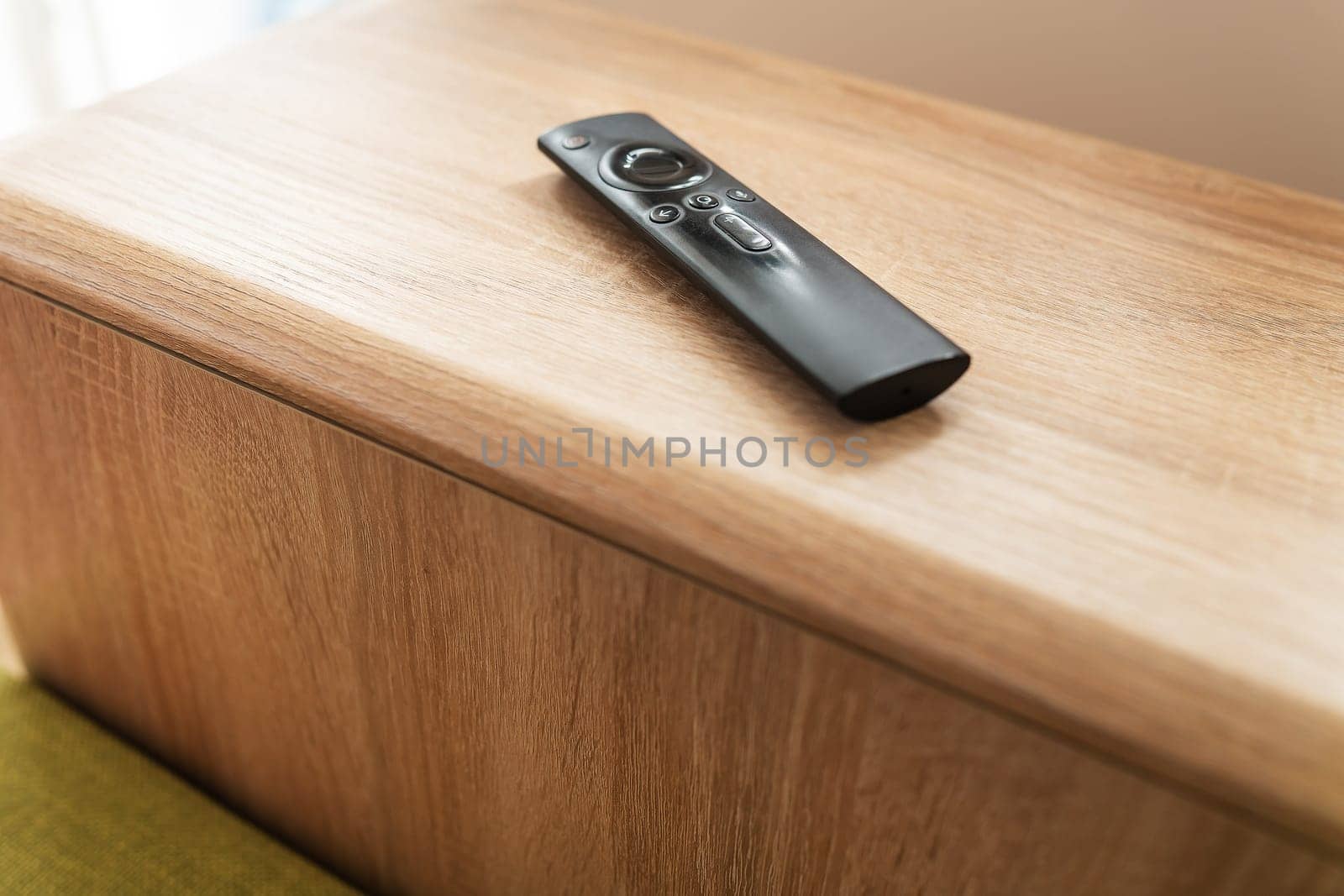 A black remote control on a wooden surface. The remote is in focus and the background is blurred