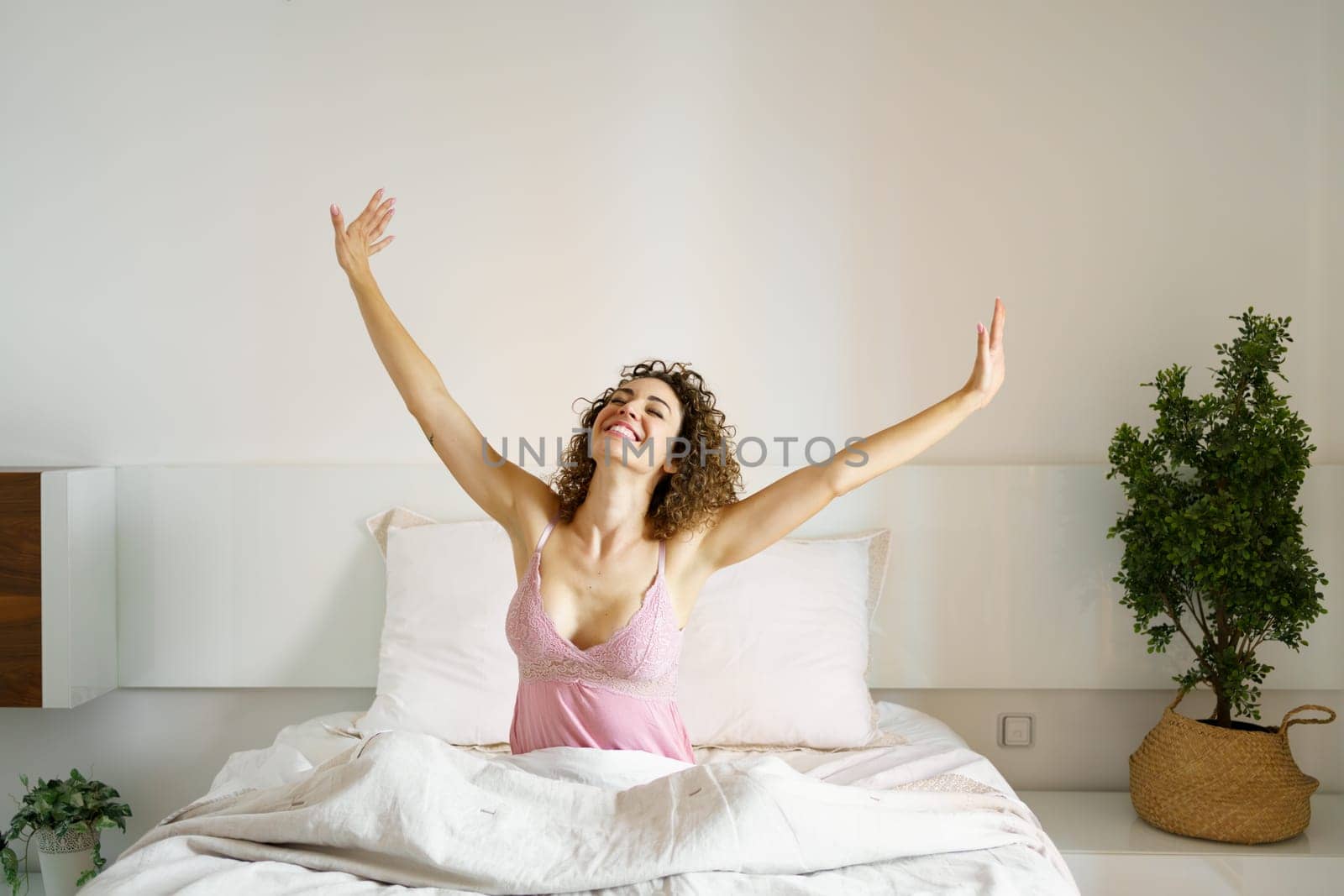 Cheerful woman sitting on bed in sleepwear by javiindy