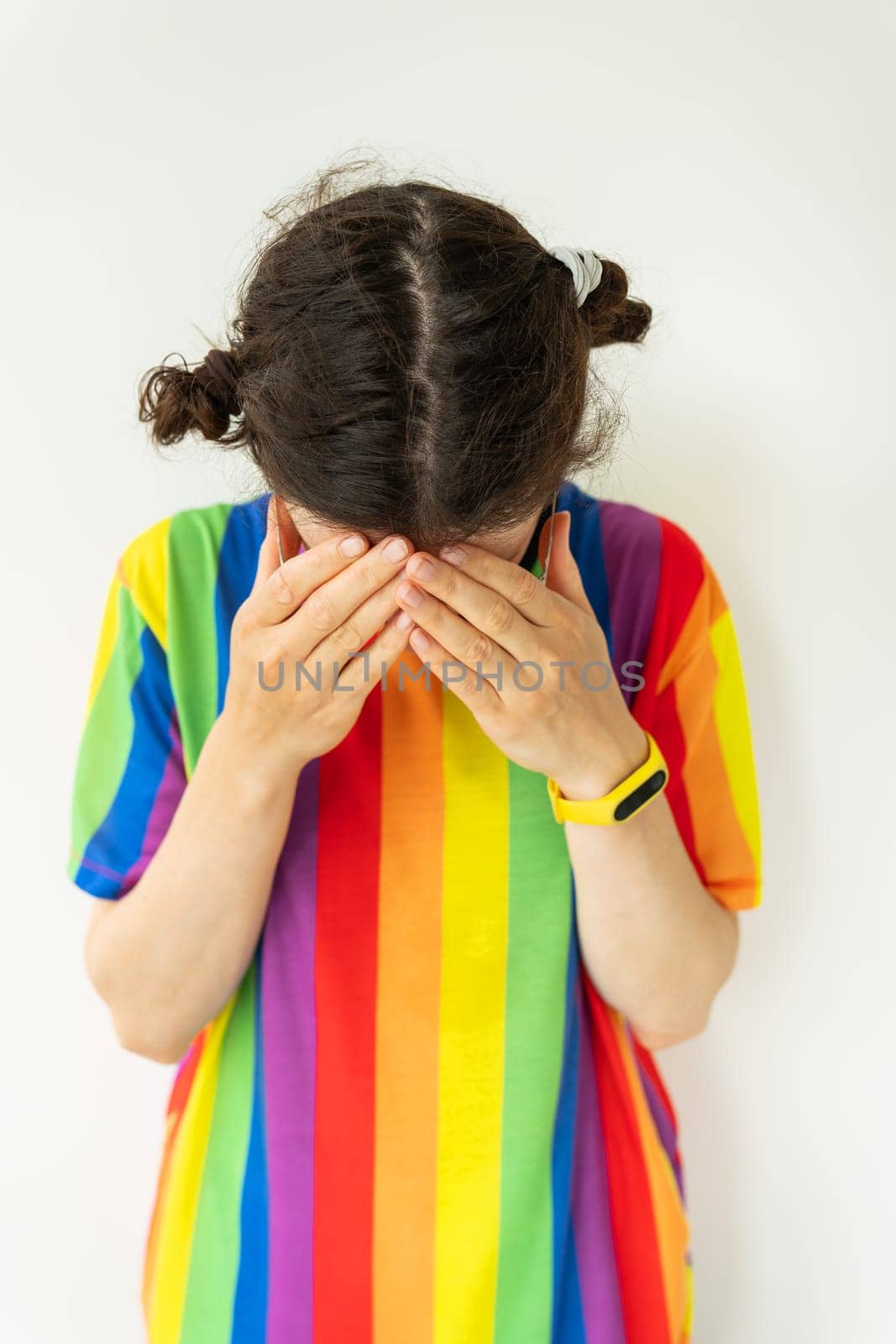 This is a portrait of a girl dressed in a shirt with a rainbow covering their face with her hands. The background is white. The mood of the image is sad or upset. by sfinks