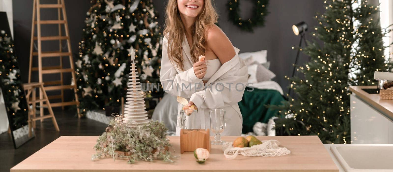 Woman Kitchen Christmas decor in white shirt, peeling tangerines. Illustrating New Year's mood holiday preparations by Matiunina