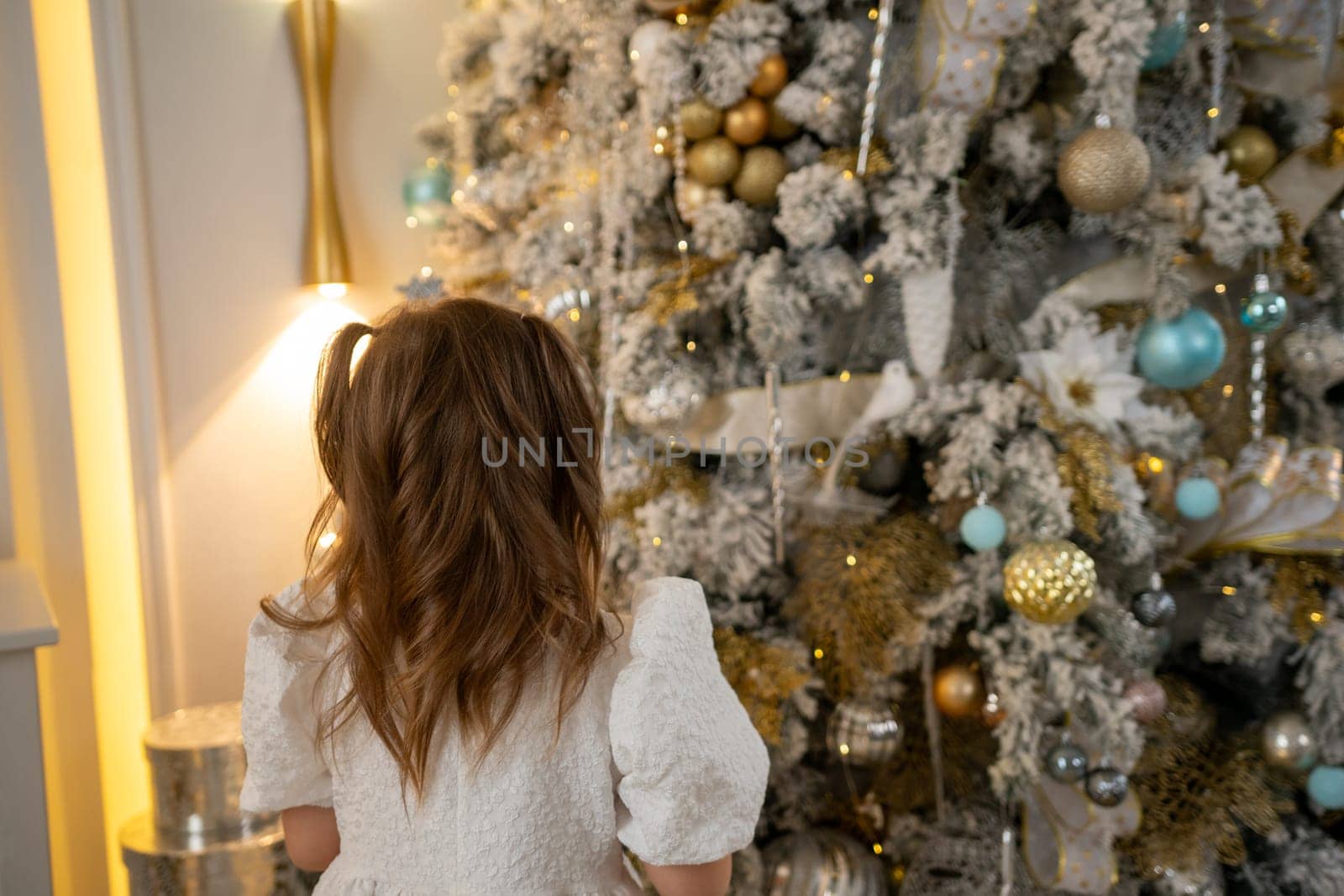 A girl in a white dress decorates a Christmas tree with her own hands, Christmas holidays at home