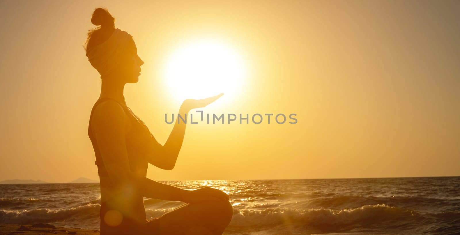 Side view of backlight and silhouette of young woman holding sun on the beach at sunrise or sunset. Spiritual practices in nature by yanik88