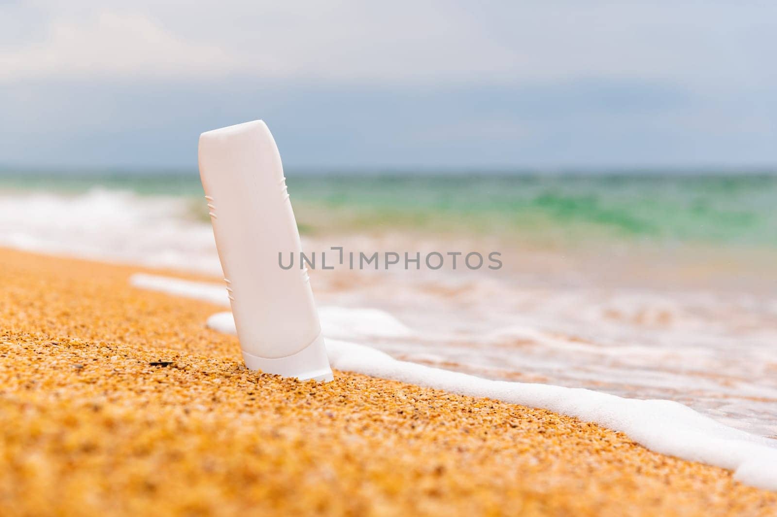 Empty tube of cream. Bottle with empty label on golden sand close-up. Cosmetic packaging mockup. Natural skin care product for your beauty routine. Summer tropical vacation mood.