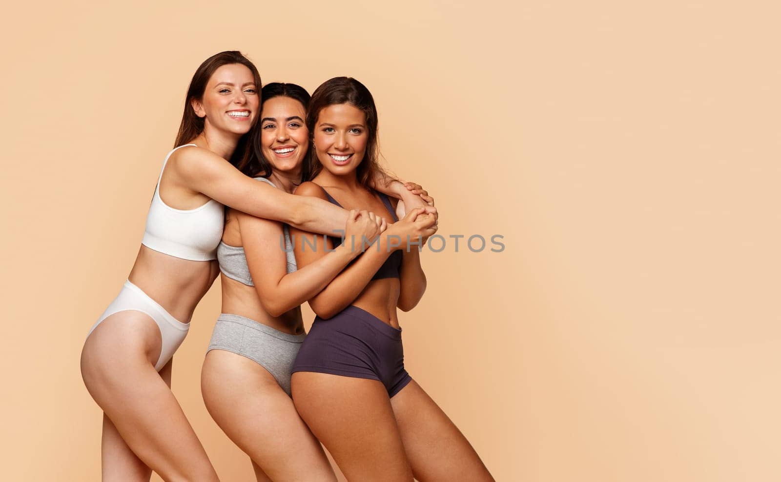 Smiling diverse young women in sports underwear enjoy friendship, diverse beauty, and body positivity, isolate on light background. Unity in diversity, friendship, body care