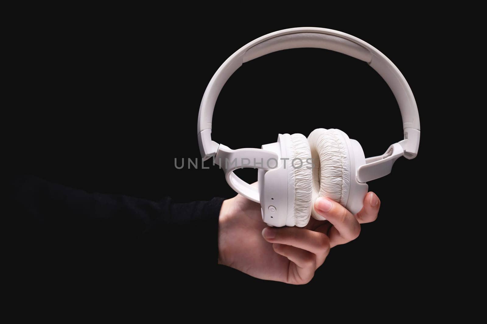 A woman hand holds large white headphones on a black background. A girl holds out wireless headphones to the camera, close-up