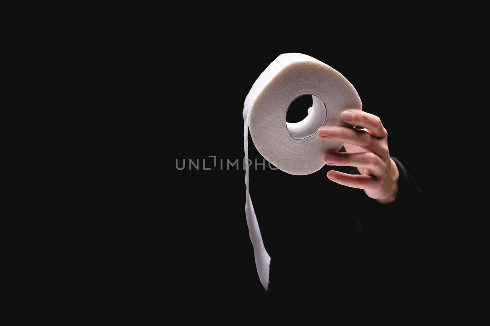 Close-up of a woman's hand using toilet paper, against a dark background. A hand holds a roll of paper. White roll of toilet paper in a woman's hand.