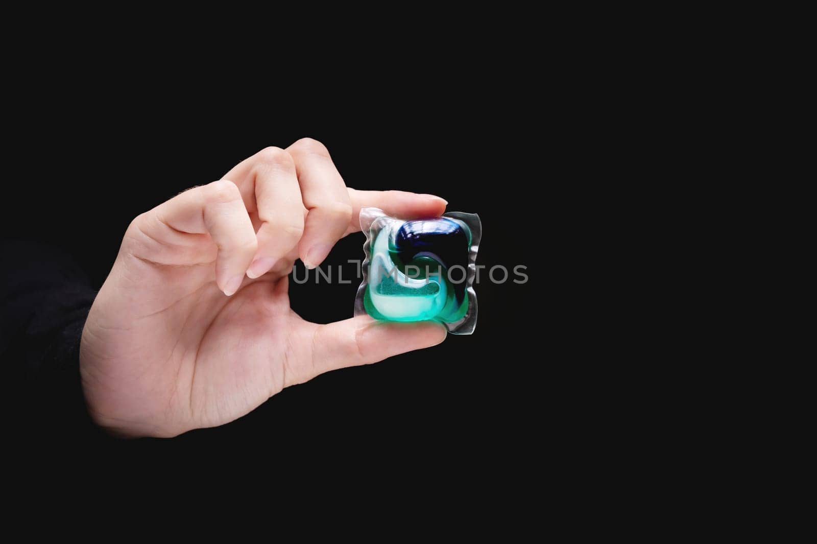 Cropped view of woman's hand holding laundry capsule on dark background, close-up.