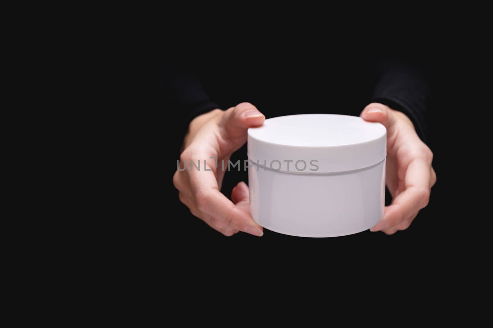 Front view of model hand holding cosmetic jar on black background for cosmetic advertising.