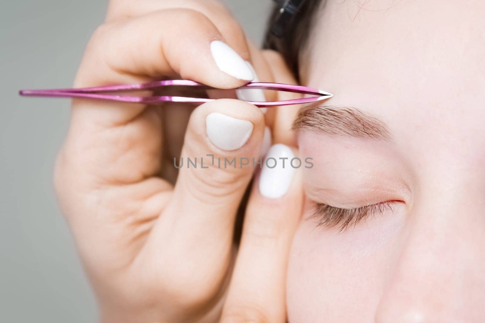 makeup artist plucks the eyebrows of a woman without makeup with tweezers. Beautiful eyebrows close-up. Professional makeup and cosmetological skin care by yanik88