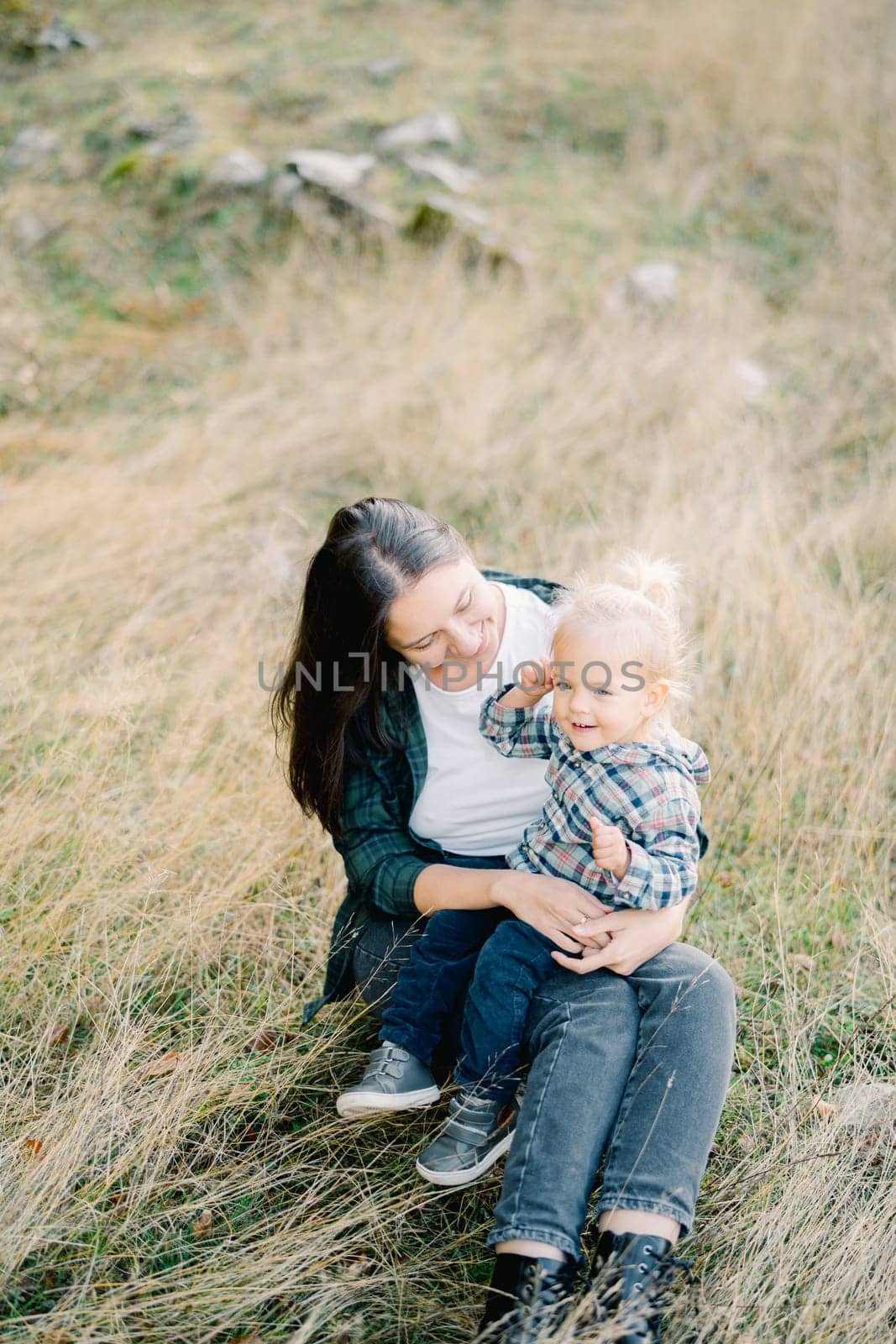 Little girl sitting on the lap of a smiling mother on the lawn. High quality photo