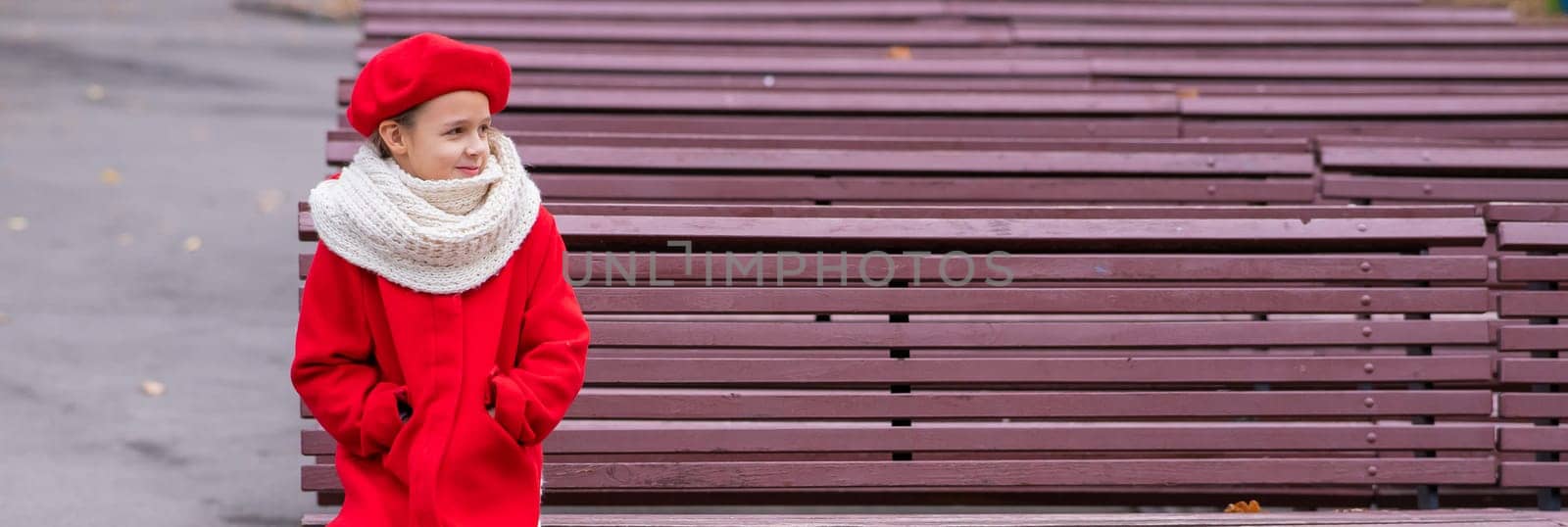 Smiling caucasian girl in a red coat and beret sits alone on a bench. by mrwed54
