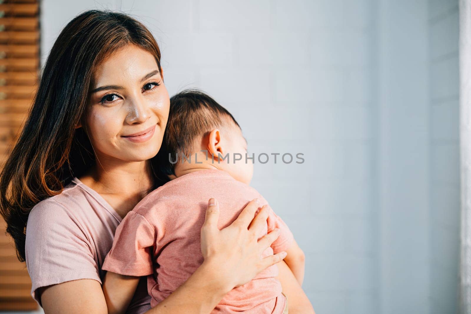 In loving embrace of their home affectionate Asian mom leans in to cuddle her peacefully sleeping infant celebrating heartwarming family moment filled with awe of new life and the joys of parenthood.