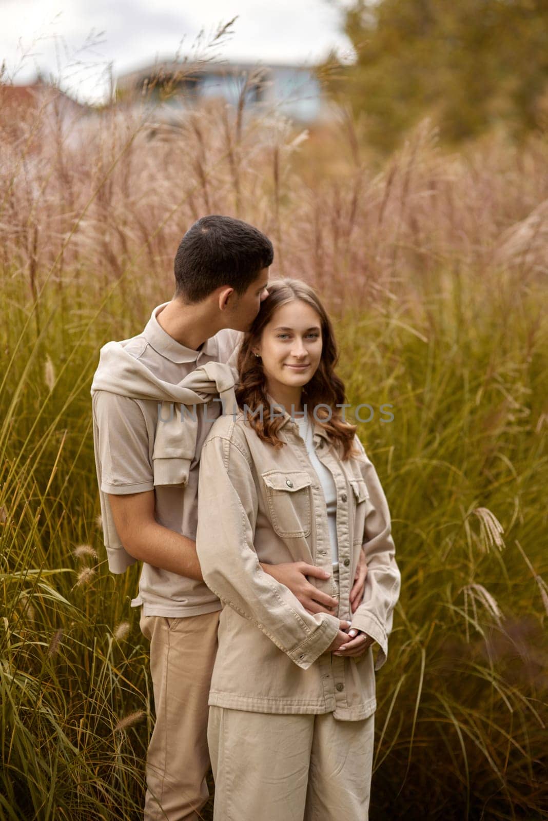 Happy couple on autumn walk outdoors. Two lovers in autumn park. Love and tender touch. Gentle hugs. Young man and woman in classic autumn colors outfit on a romantic date in a cozy park. Young girl and guy with blond hair kisses, show love, affection. Boy and girl of European appearance with warm clothes, pictures with soft background bokeh blur fall. Concept of happiness, joy by Andrii_Ko