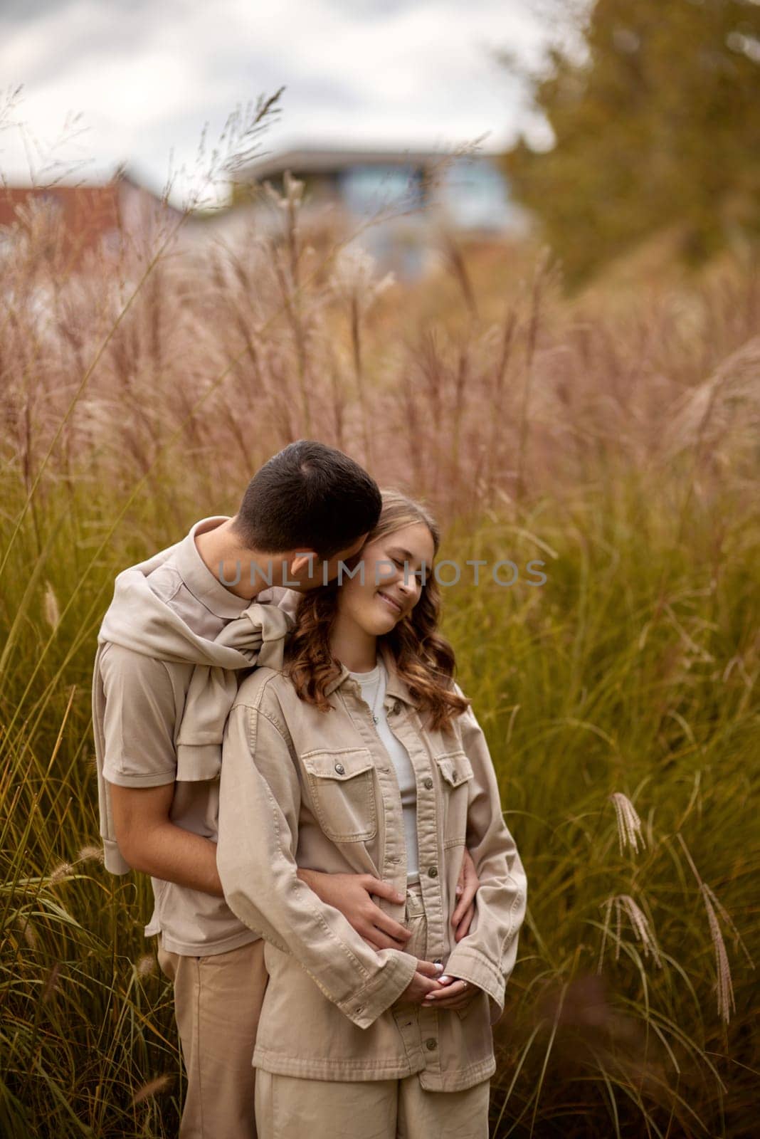 Happy couple on autumn walk outdoors. Two lovers in autumn park. Love and tender touch. Gentle hugs. Young man and woman in classic autumn colors outfit on a romantic date in a park. Young girl and guy with blond hair kisses, show love, affection. Boy and girl of European appearance with warm clothes, pictures with soft background bokeh blur fall. Concept of happiness,