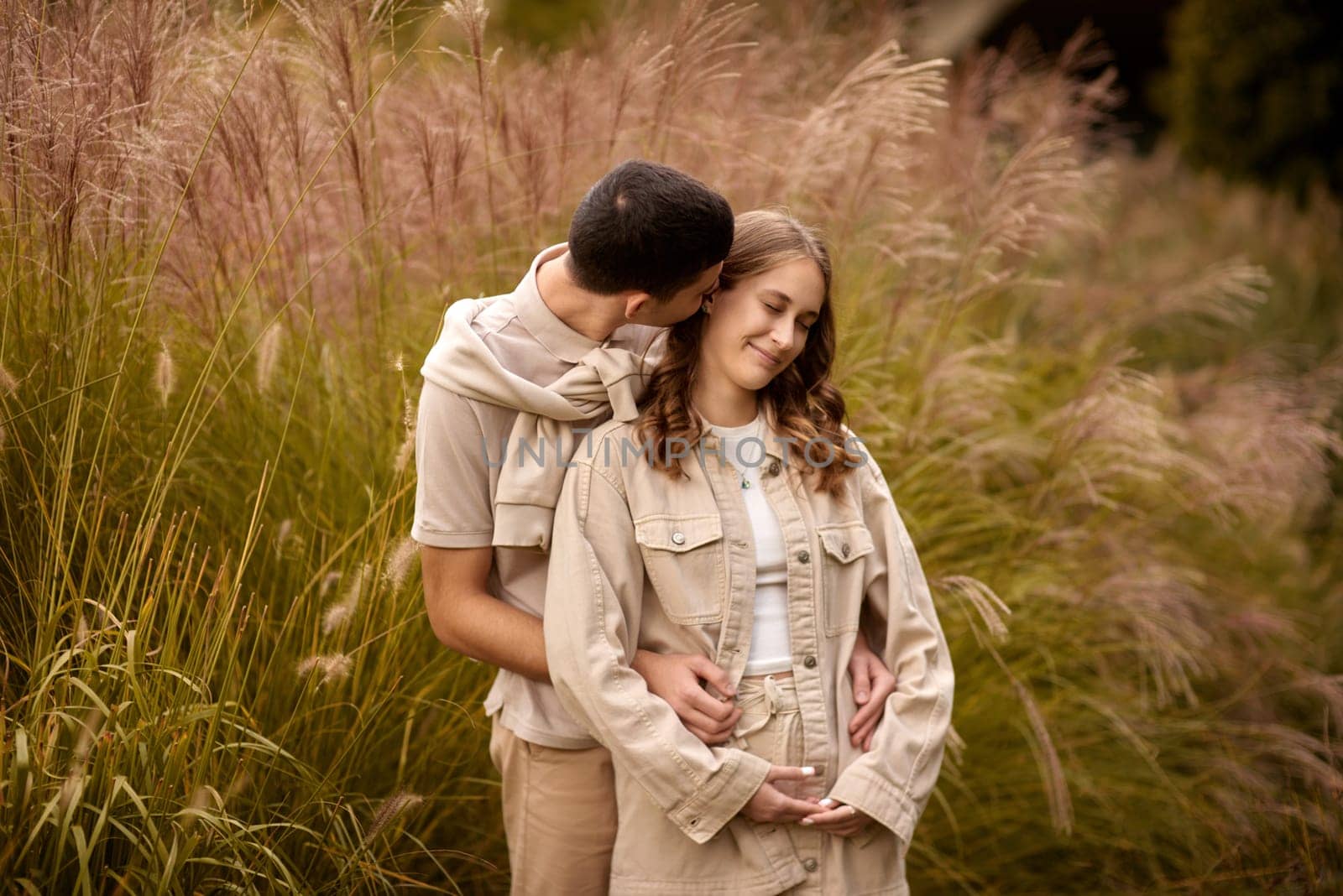 Happy couple on autumn walk outdoors. Two lovers in autumn park. Love and tender touch. Gentle hugs. Young man and woman in classic autumn colors outfit on a romantic date in a cozy park. Young girl and guy with blond hair kisses, show love, affection. Boy and girl of European appearance with warm clothes, pictures with soft background bokeh blur fall. Concept of happiness, joy by Andrii_Ko