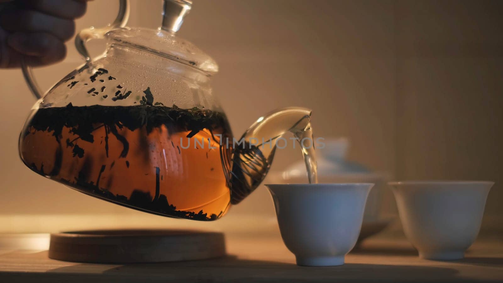 Close up of teapot with black chinese tea , gaiwan and pialas on the wooden table. Female hand poring hot beverage into the small white cups.