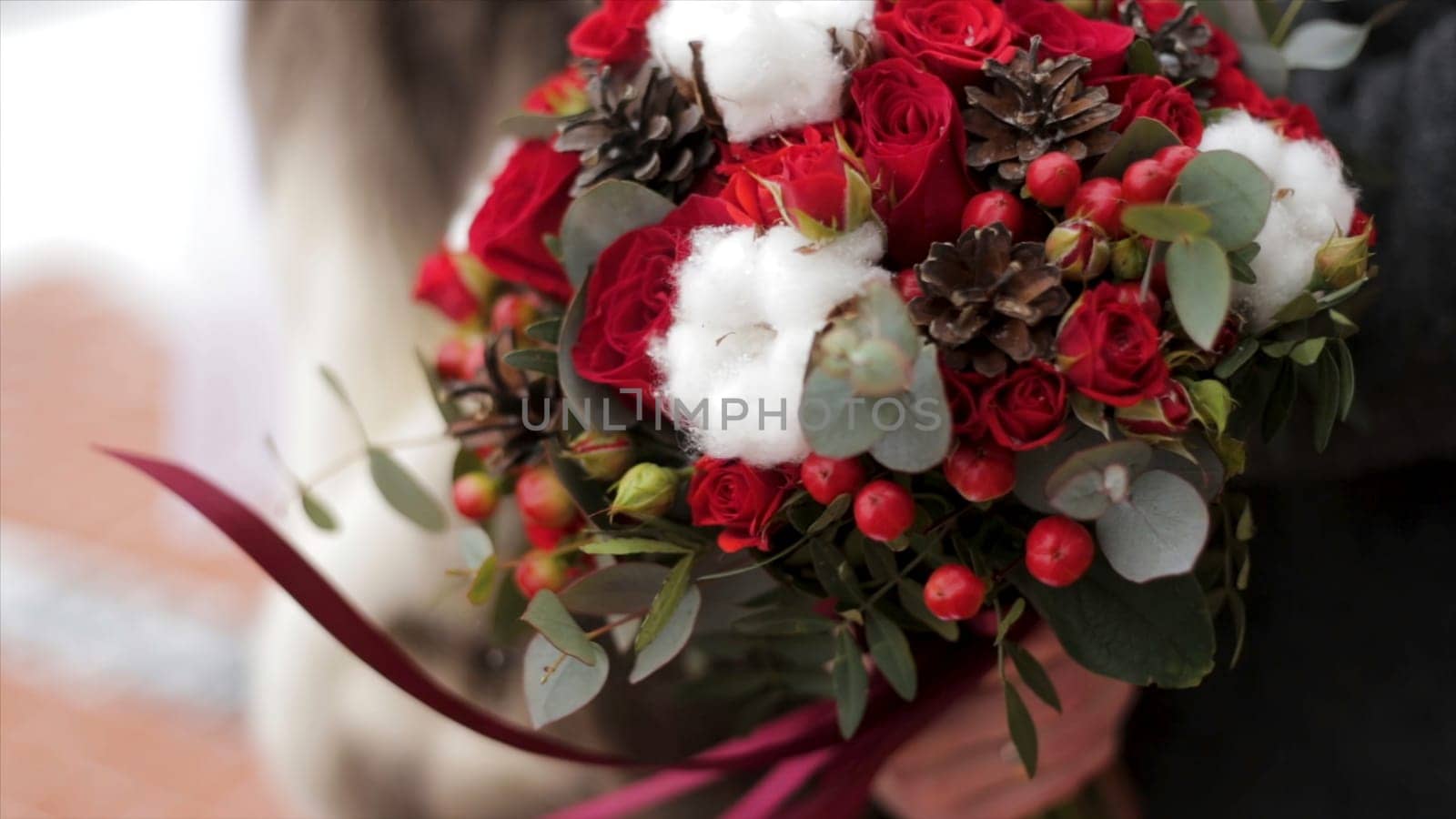 Close up of a bride holding a wedding bouquet with red roses. Bride holding flowers.